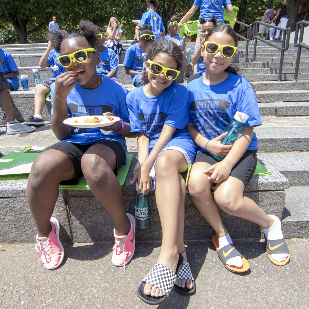 Three girls wearing sunglasses sitting next to each other, eating lunch through Boston Summer Eats