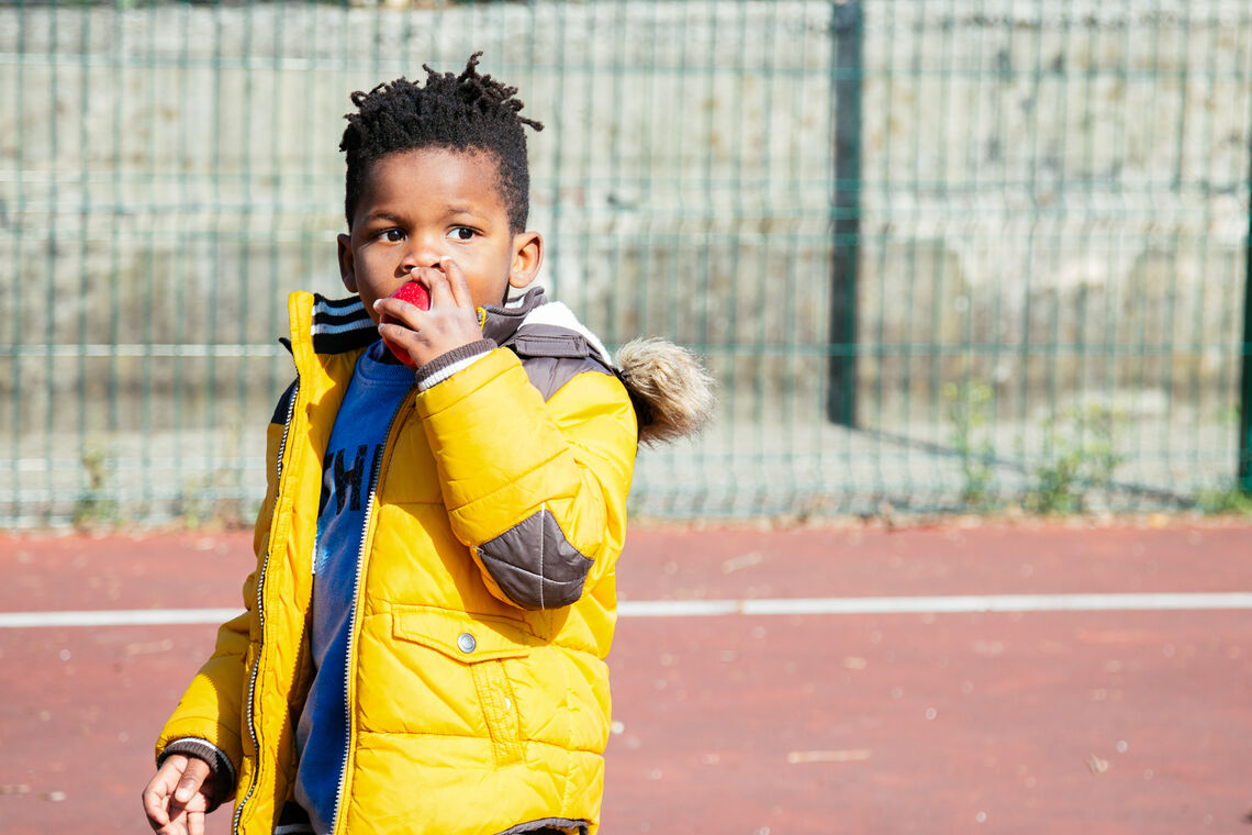 boy eating apple outside of school wearing a coat looking worried