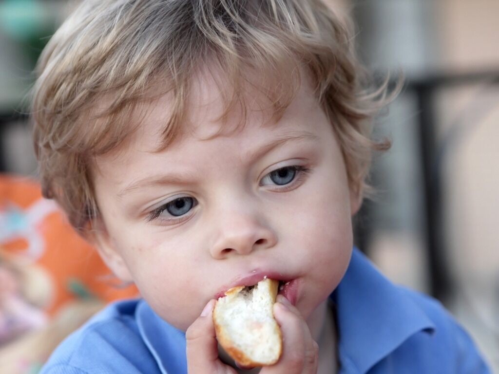 Little boy eating a piece of bread.