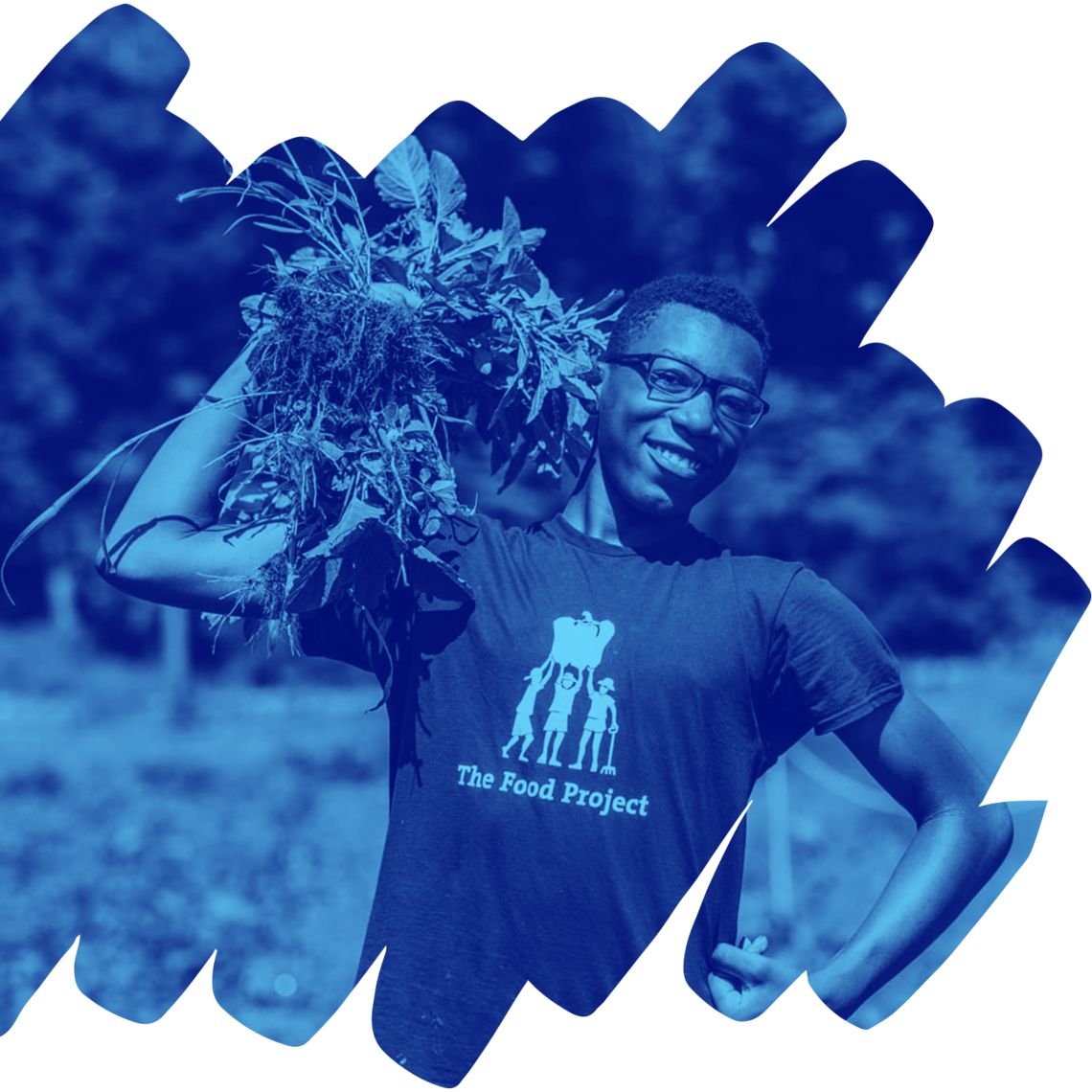 Image of a person with glasses holding harvested greens over their shoulder. Their other arm is bent with the hand making a fist against their hip. They are standing in a garden and smiling towards the camera.