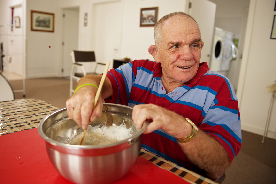 Senior disabled man stirs a bowl while he looks over his shoulder to see if he is doing it right