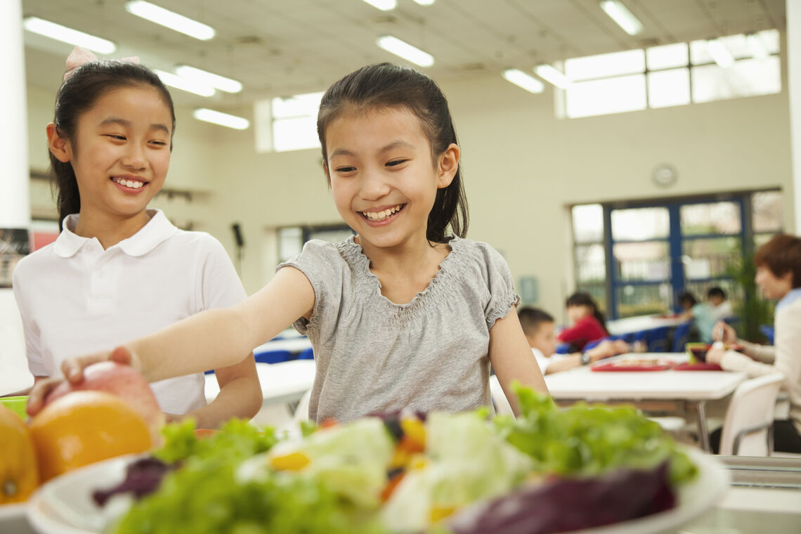 girl reaching for salad during school lunch