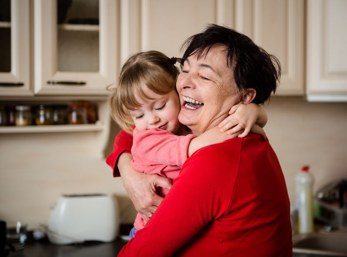 Happy senior woman hugging her beautiful grandchild - in kitchen at home