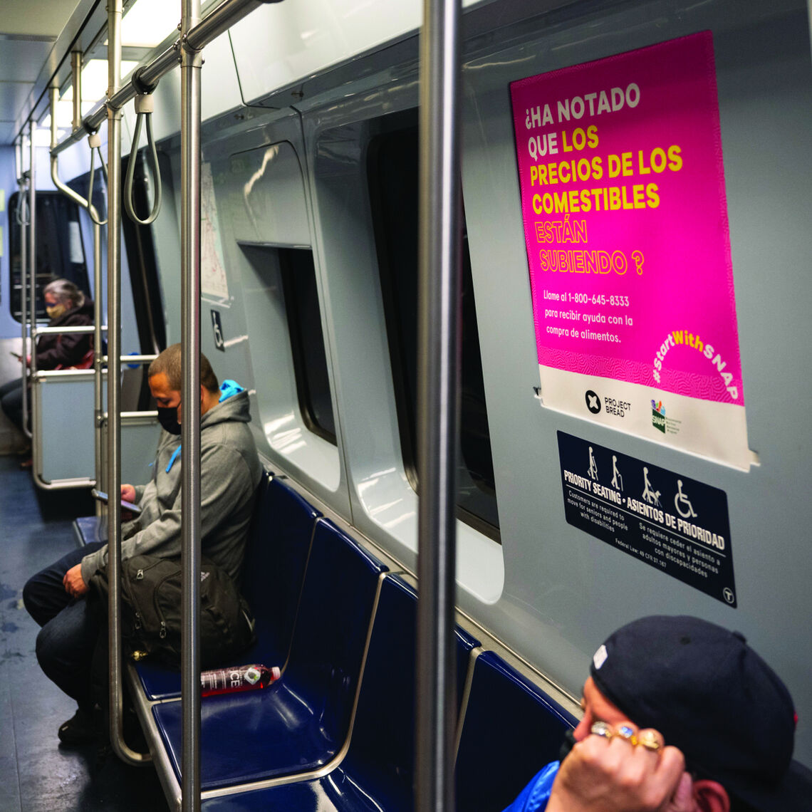 People are seated inside of a T car where an advertisement for SNAP is on the wall in Spanish