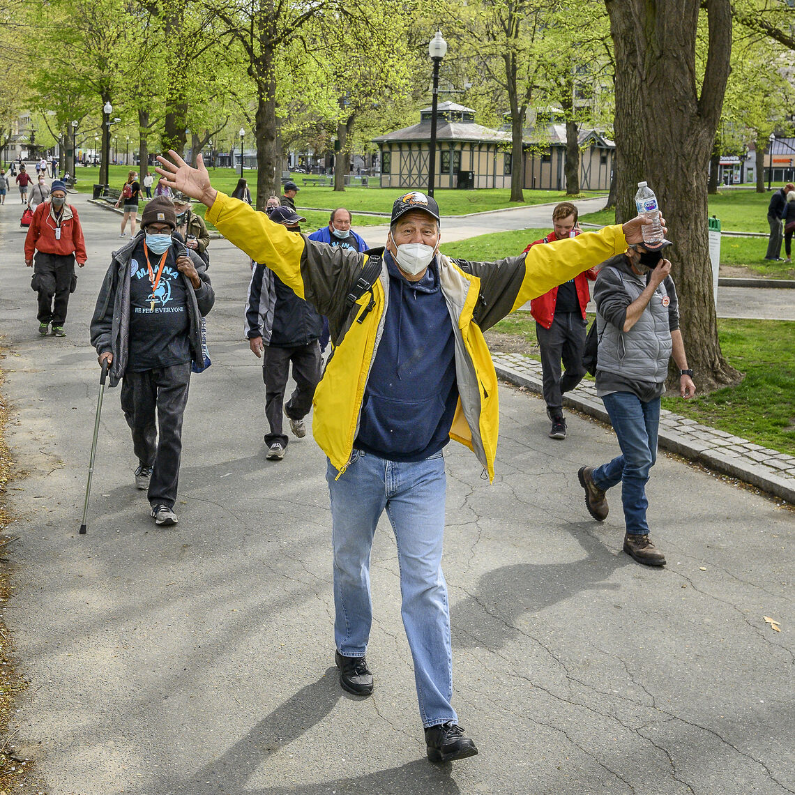 A man wearing a mask has wide open arms as he walks through Boston Common as a virtual walk with his team from Boston St. Paul's Cathedral for the 2022 virtual Walk for Hunger