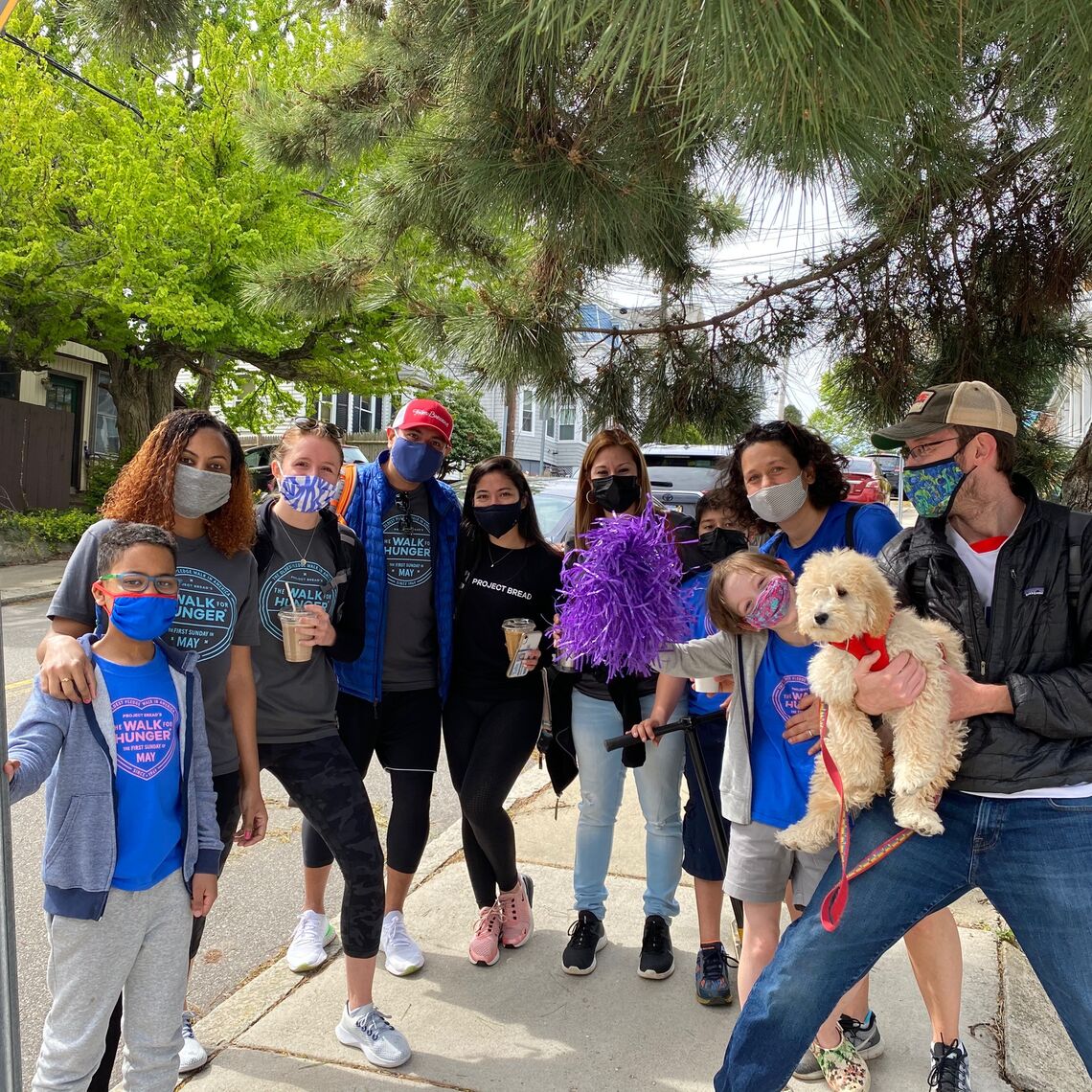 A large group of people wearing masks and Walk for Hunger shirts, and a puppy, participate virtually in 2021