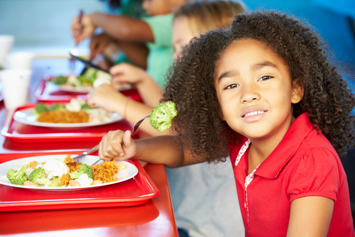 Student in red shirt eats lunch of broccoli in cafeteria