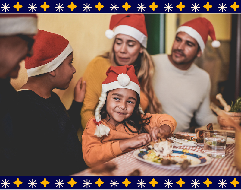 A family in Santa hats sits around the table with a meal