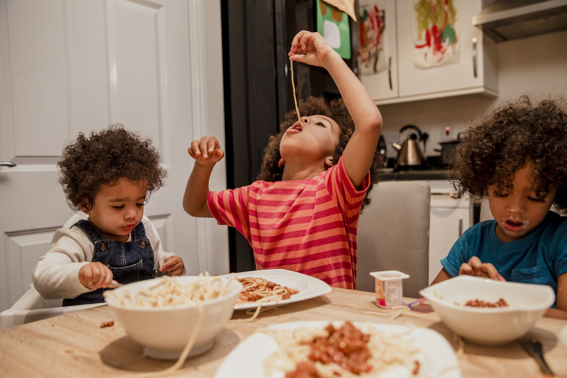 Three young brothers sit around the table eating spaghetti dinner